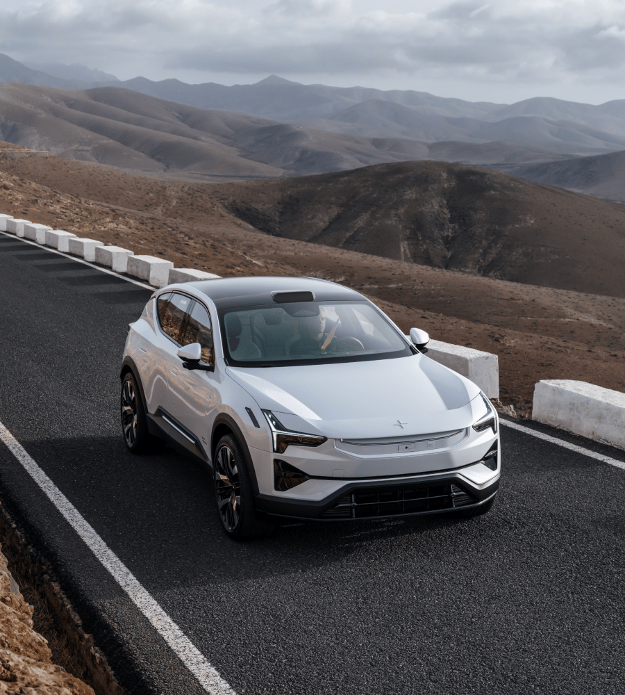 A Polestar drives on a road with mountains in the background.