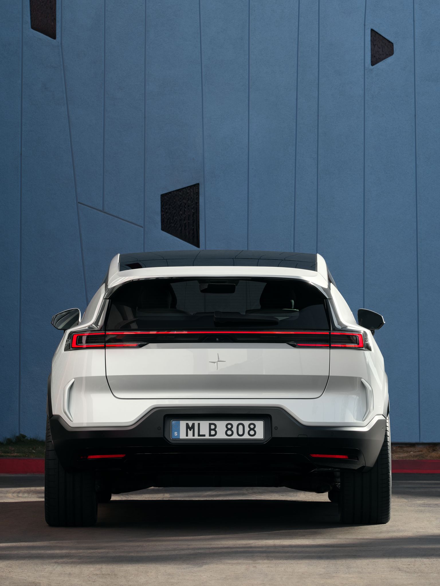 Polestar 3 seen from the back parked in front of a blue wall.